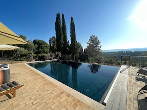Piscina azul translúcida com deck de madeira, cercada por árvores altas e vista para colinas ao longe.