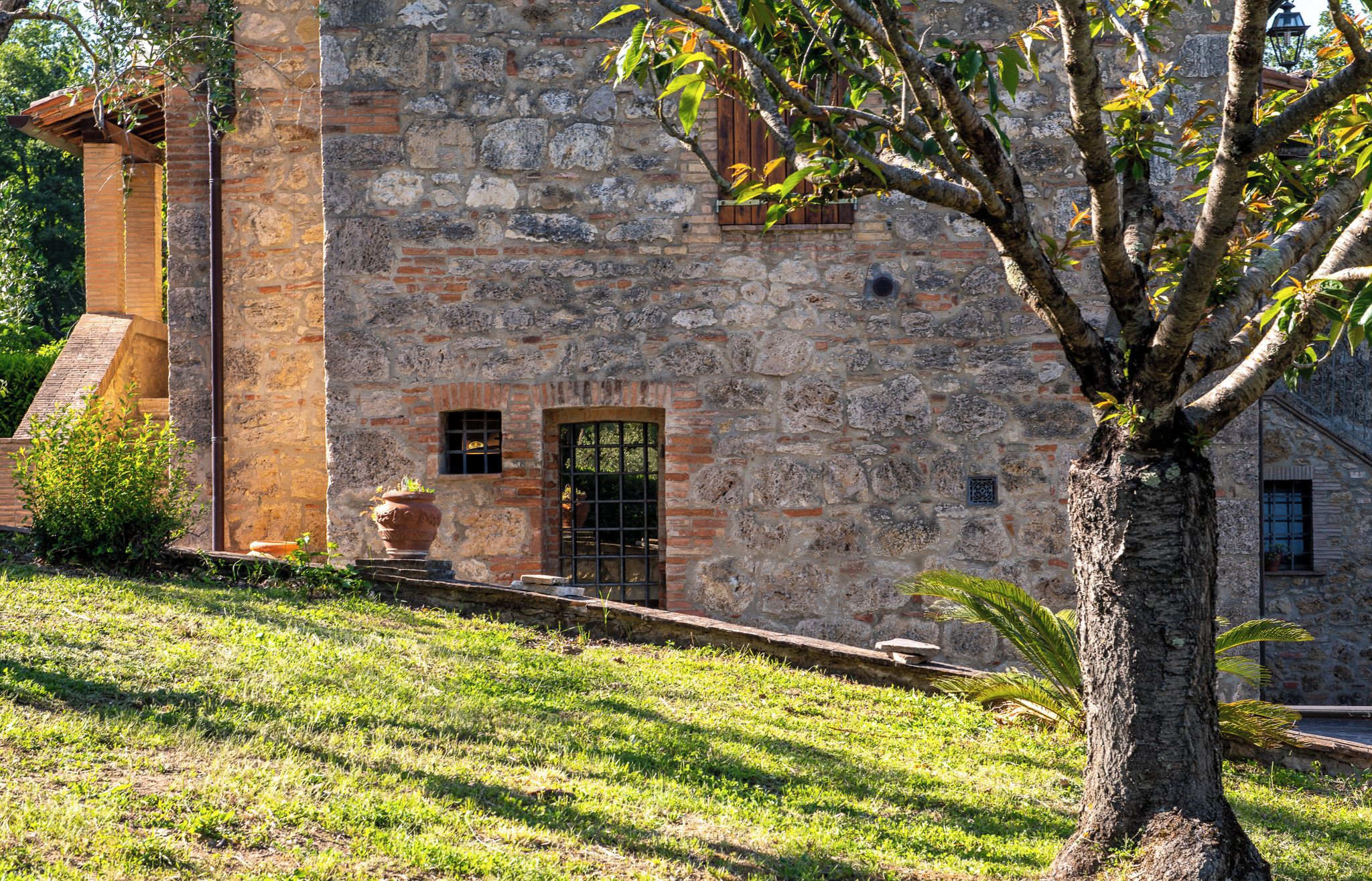 Un bâtiment en pierre avec une porte et des fenêtres en bois, entouré d’herbe et d’arbres.