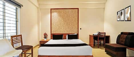 A hotel room with a bed, a desk, a chair, a sofa, a ceiling fan, and a window with blinds.