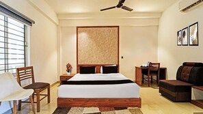 A hotel room with a bed, a desk, a chair, a sofa, a ceiling fan, and a window with blinds. - Deluxe Room Ram Vikram Residency (Coimbatore)
