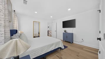 Een slaapkamer met een bed, een dressoir, een televisie en een spiegel.
