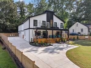 A modern two-story house with a covered porch, a driveway, and a fenced backyard.
