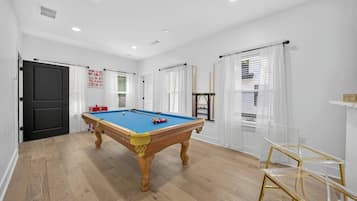 Een pooltafel in een ruimte met witte muren, houten vloeren en een deur.