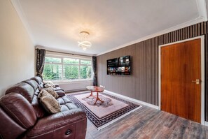 Ein Wohnzimmer mit einer Ledersofa, einem Couchtisch, einem an der Wand befestigten Flachbildfernseher und einer Holztür.