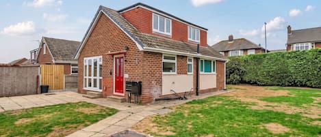 A two-story brick house with a red door, a visible garage, and a well-maintained lawn.