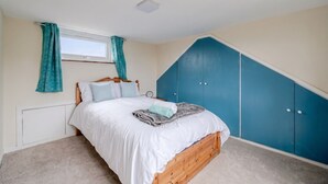 Un dormitorio con cama, ventana con cortinas, radiador y un armario azul.