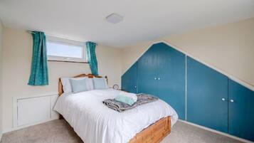 A bedroom with a bed, a window with curtains, a radiator, and a blue wardrobe.
