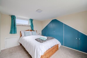 Ein Schlafzimmer mit einem Bett, einem Fenster mit Vorhängen, einem Heizkörper und einem blauen Kleiderschrank.