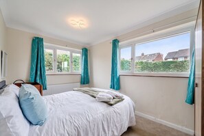 Un dormitorio con cama, radiador, ventana y cortinas.
