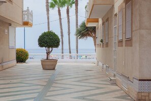A corridor with a tiled floor, a potted tree, and a view of the sea.