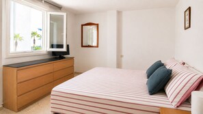 A bedroom with a bed, a dresser, a television, a mirror, and a window with a view of palm trees.