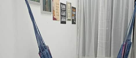 A room with a blue hammock, a window with sheer curtains, and several framed motivational posters on the wall.