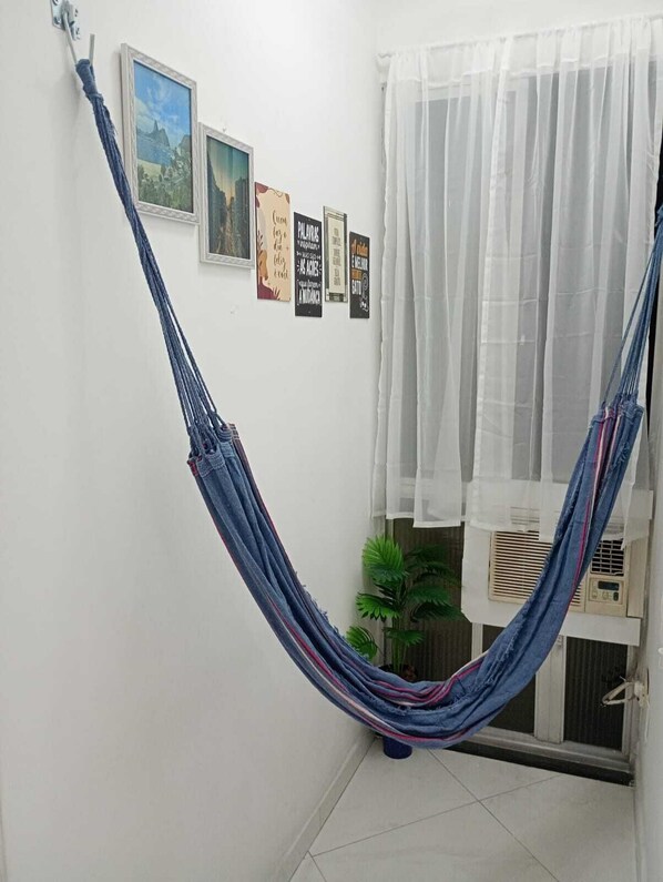 A room with a blue hammock, a window with sheer curtains, and several framed motivational posters on the wall.