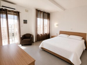 A hotel room with a bed, a chair, a desk, and a window with curtains. - Sliema 2BR Sea View Apartment Qui Si Sana with Terrace & BBQ (Sliema)