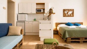Un espacio habitable compacto con kitchenette, una cama con manta verde, un sofá azul y un pequeño comedor.