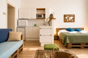 Ein kompakter Wohnbereich mit Küchenzeile, einem Bett mit grüner Decke, einem blauen Sofa und einem kleinen Essbereich.