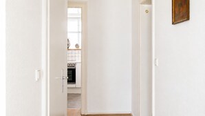 Un pasillo que conduce a una cocina con paredes blancas, una puerta con pomo dorado y un cuadro enmarcado en la pared.