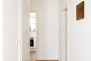 Ein Flur, der zu einer Küche führt, mit weißen Wänden, einer Tür mit goldener Klinke und einem gerahmten Bild an der Wand.