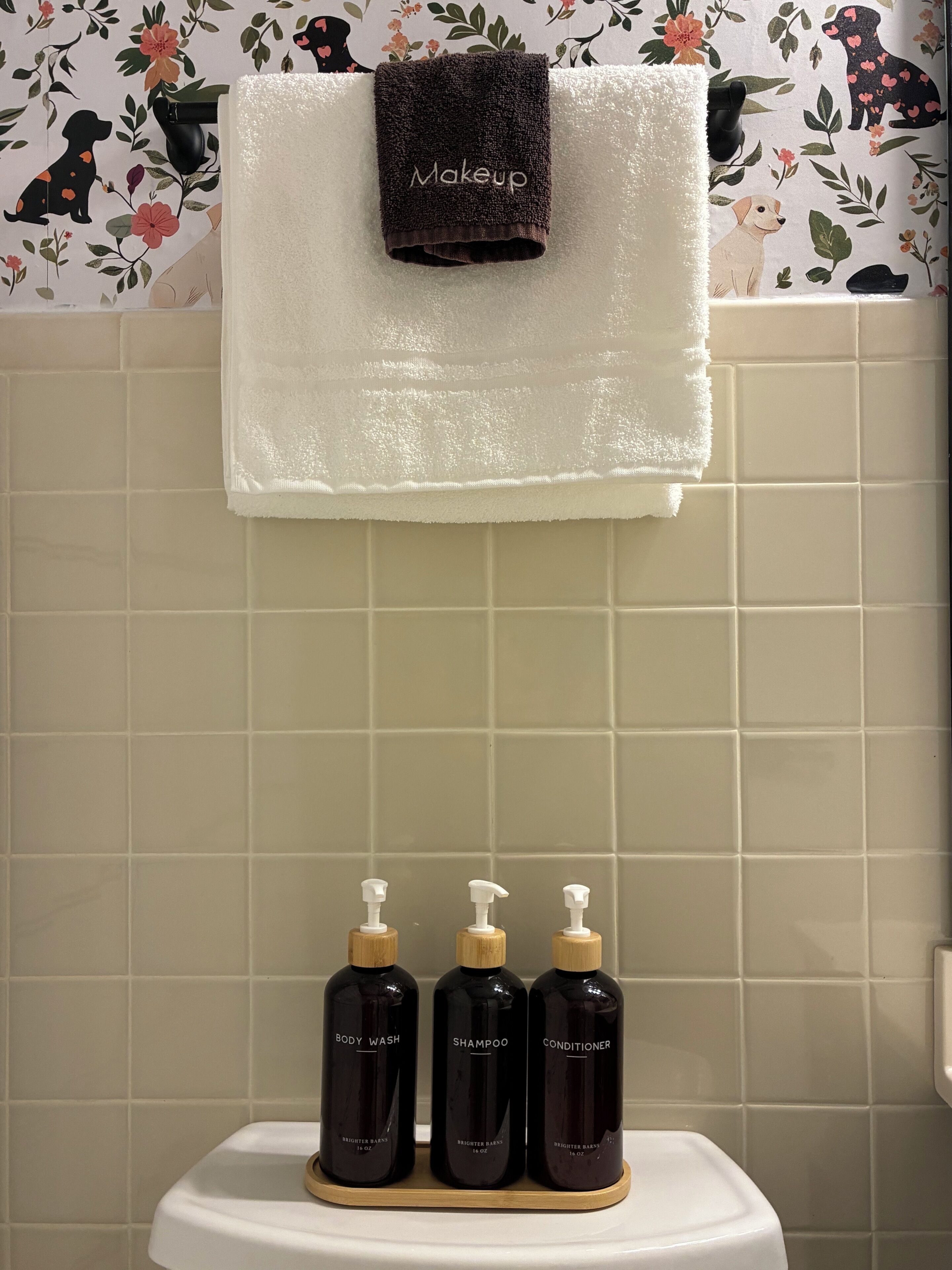 Ein Badezimmer mit einer weißen Toilette, einem Handtuchhalter mit einem dunklen Handtuch und drei Brightener Bars auf einer Holztablett.