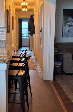 A hallway with a kitchen area featuring a bar stool seating arrangement, a dining table, and a couch in the adjacent living area. - The Summit at 4848-3 Bedrooms, Steps to the Snowshoe Village and Slopes! (Snowshoe)