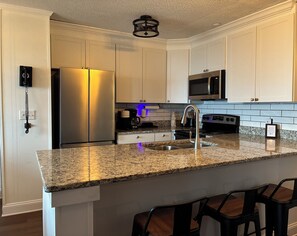A modern kitchen with white cabinetry, a stainless steel refrigerator, a built-in microwave, a granite countertop, and a bar area with stools. - The Summit at 4848-3 Bedrooms, Steps to the Snowshoe Village and Slopes! (Snowshoe)