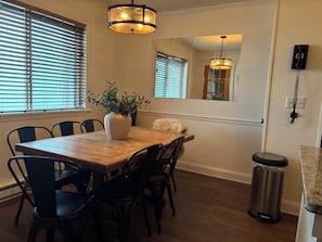 A dining area with a wooden table, black chairs, a white vase with plants, and a hanging light fixture. - The Summit at 4848-3 Bedrooms, Steps to the Snowshoe Village and Slopes! (Snowshoe)