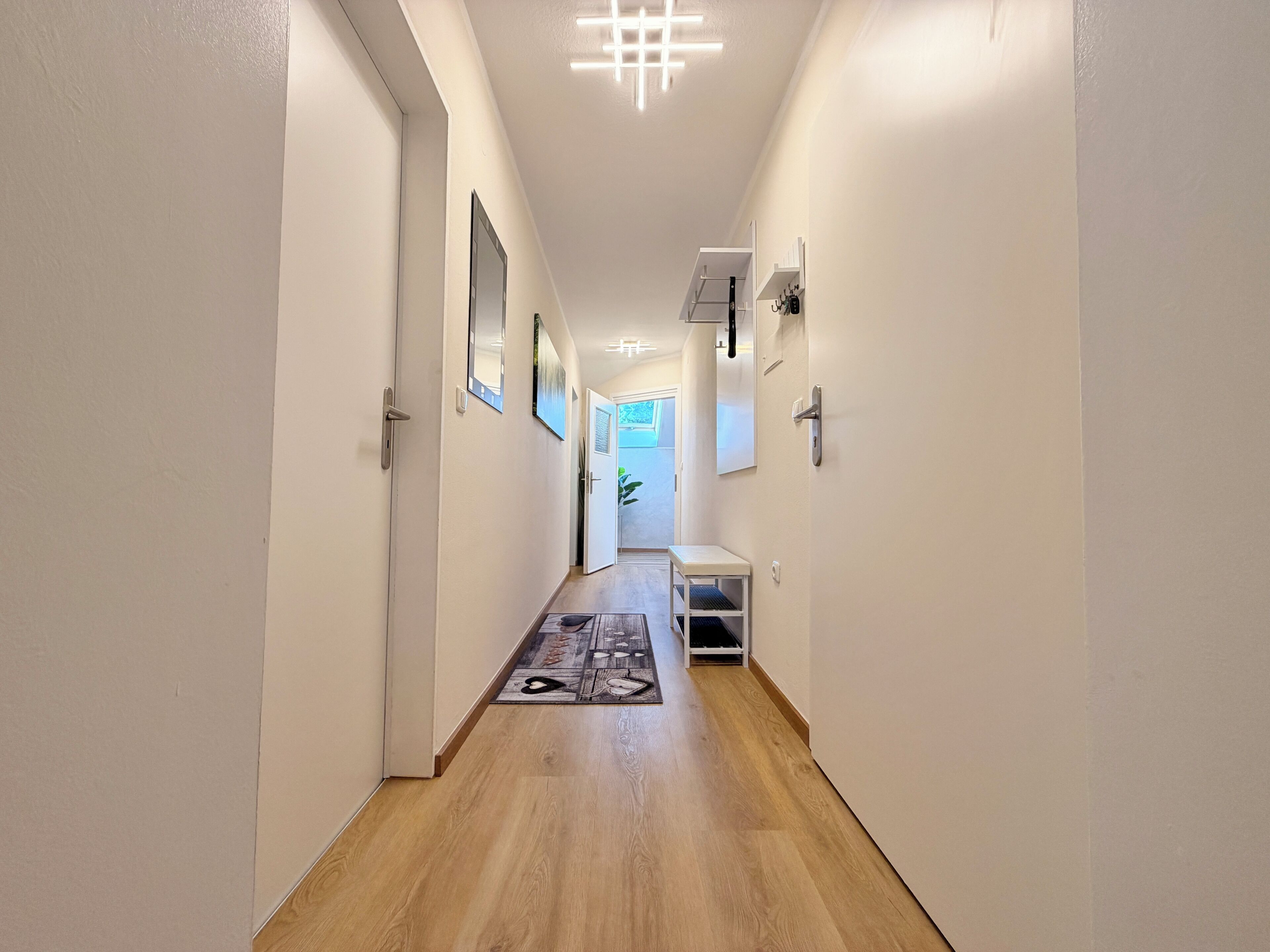 A hallway with a wooden floor, white walls, and a ceiling light fixture.