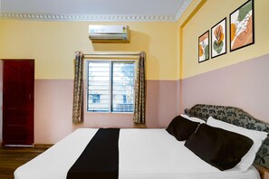 A hotel room with a bed, a window with curtains, an air conditioning unit, and wall art. - Deluxe Mayuri Lodge (Bagepalli)