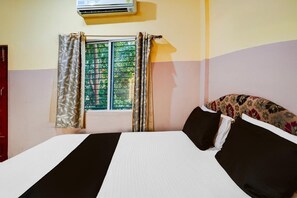 A room with a bed, a window with curtains, and an air conditioning unit. - Deluxe Mayuri Lodge (Bagepalli)