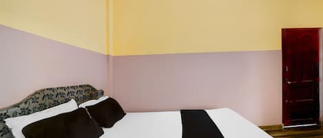 A room with a bed, a floral-patterned sofa, and a red door.