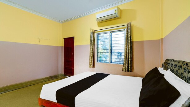 A hotel room with a bed, a window with curtains, an air conditioning unit, and a red wardrobe. - Deluxe Mayuri Lodge (Bagepalli)