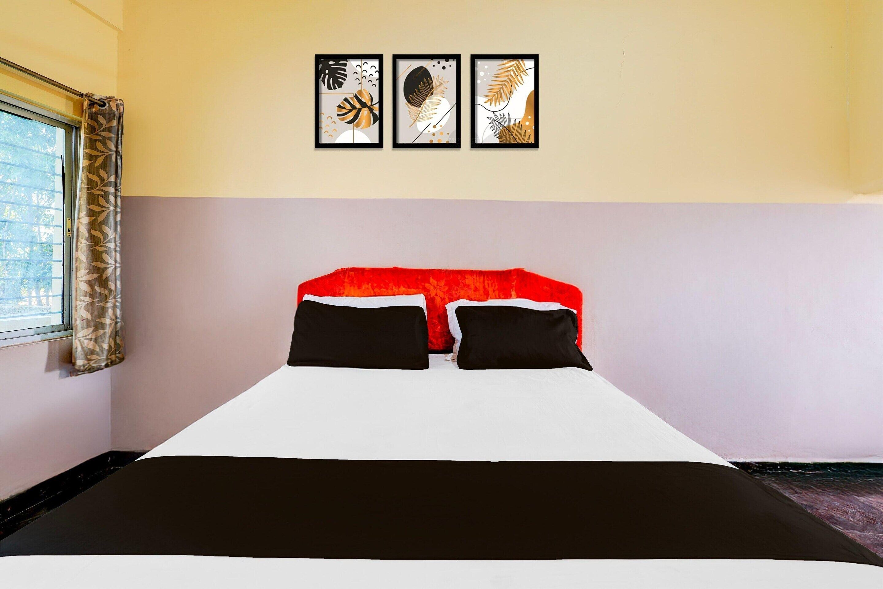 A hotel room with a bed, a window with curtains, and three framed artworks on the wall.