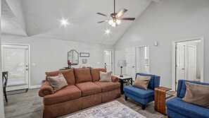 A spacious living room with a brown sofa, a blue sofa, and a wooden coffee table. There is a ceiling fan and a large mirror on the wall.