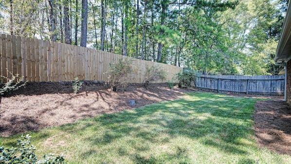 A backyard with a wooden fence, a grassy lawn, and a tree line in the background.
