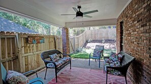 Ein überdachter Patio-Bereich mit zwei Korbstühlen, einem Deckenventilator und Blick auf einen Garten.