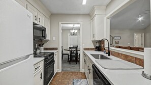 Cocina compacta con muebles blancos, microondas, estufa y pileta.