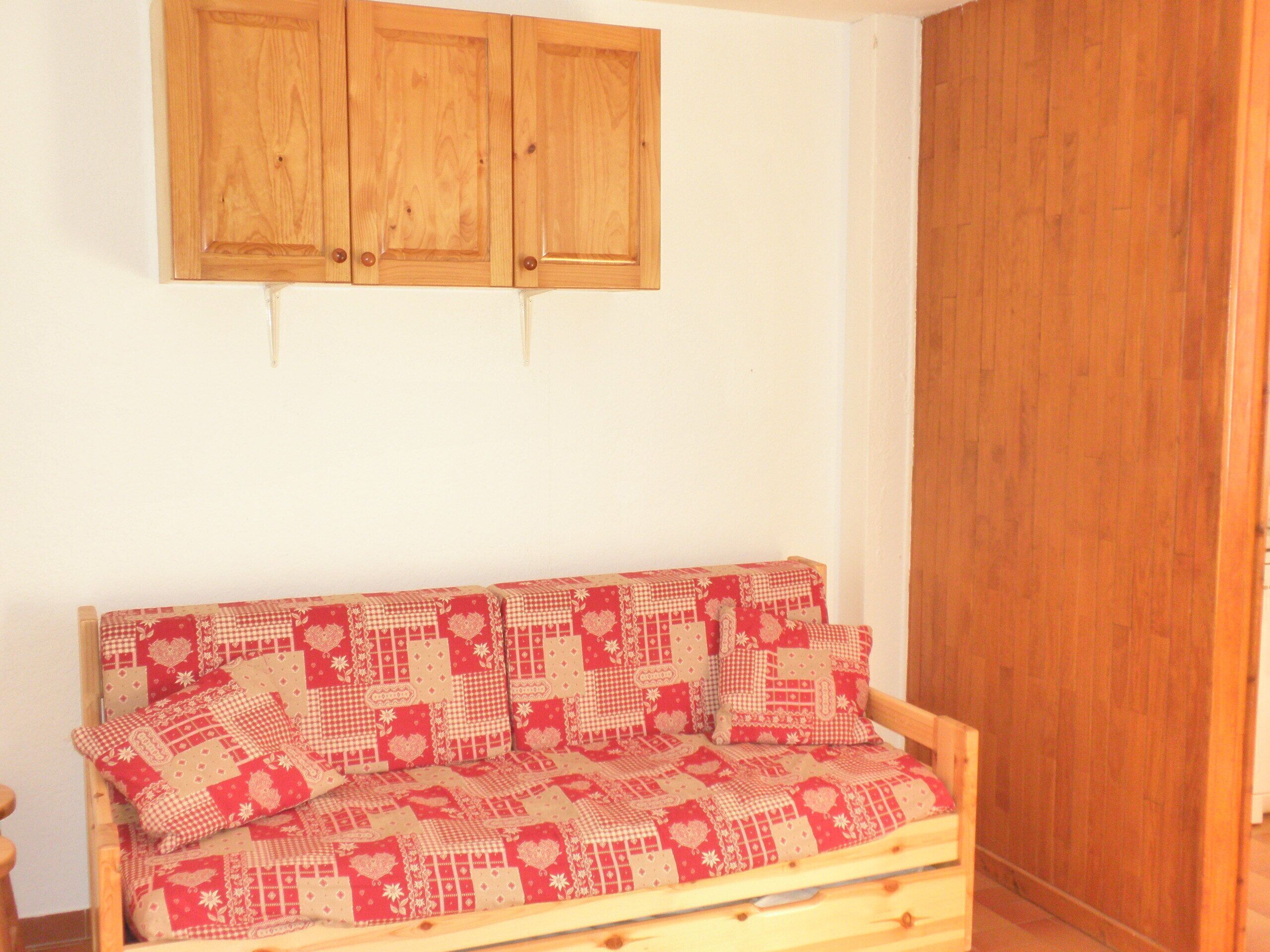 Ein Holzsofa mit kariertem Kissenmuster, ein Holzschrank darüber und eine Holztür zur rechten Seite.