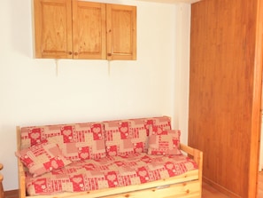 A wooden sofa with a checkered cushion pattern, a wooden cabinet above it, and a wooden door to the right. - Studio for 4 people in Vars, right at the base of the slopes (Vars)