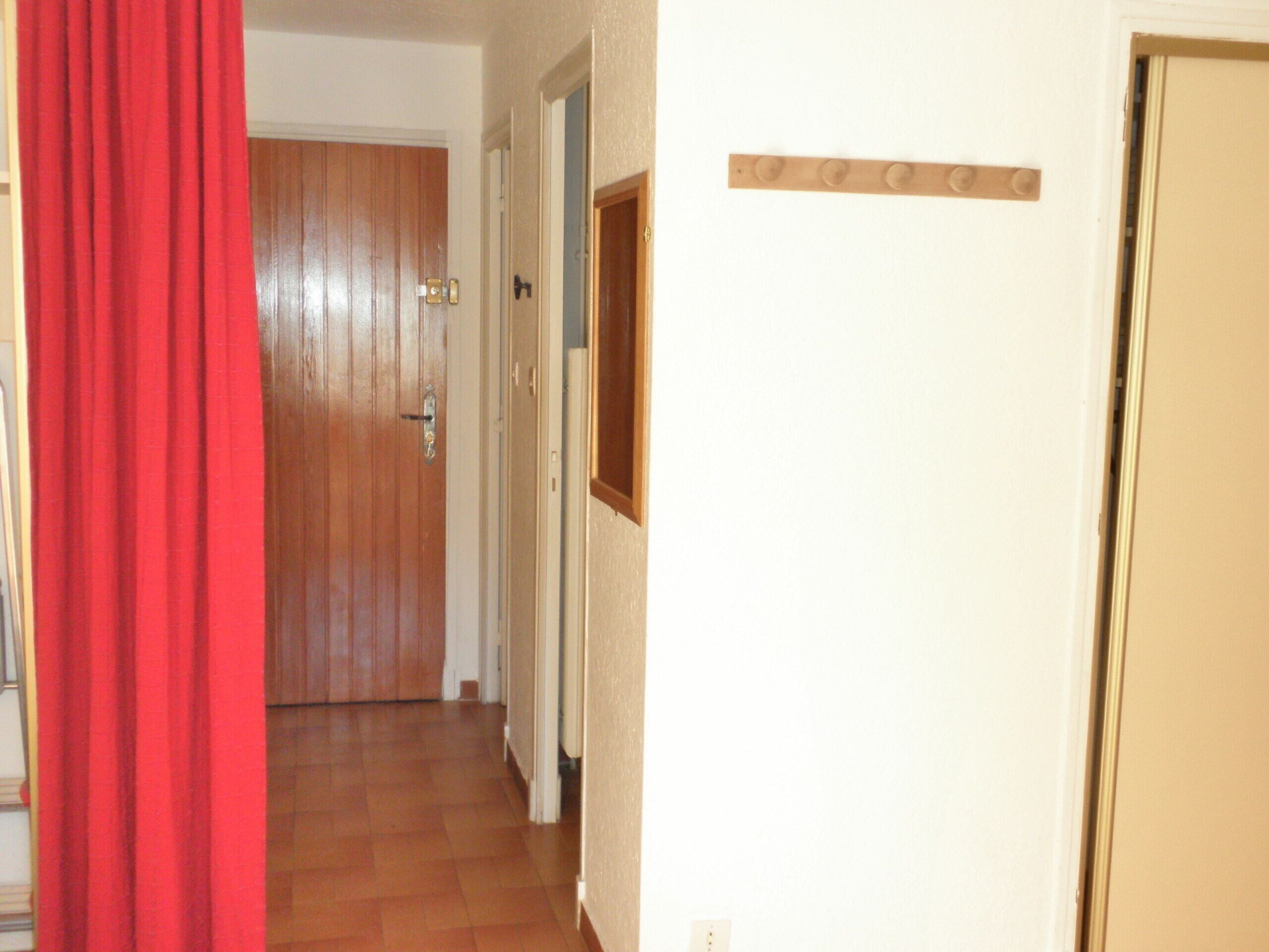 A hallway with a wooden door, a red curtain, and a coat rack.