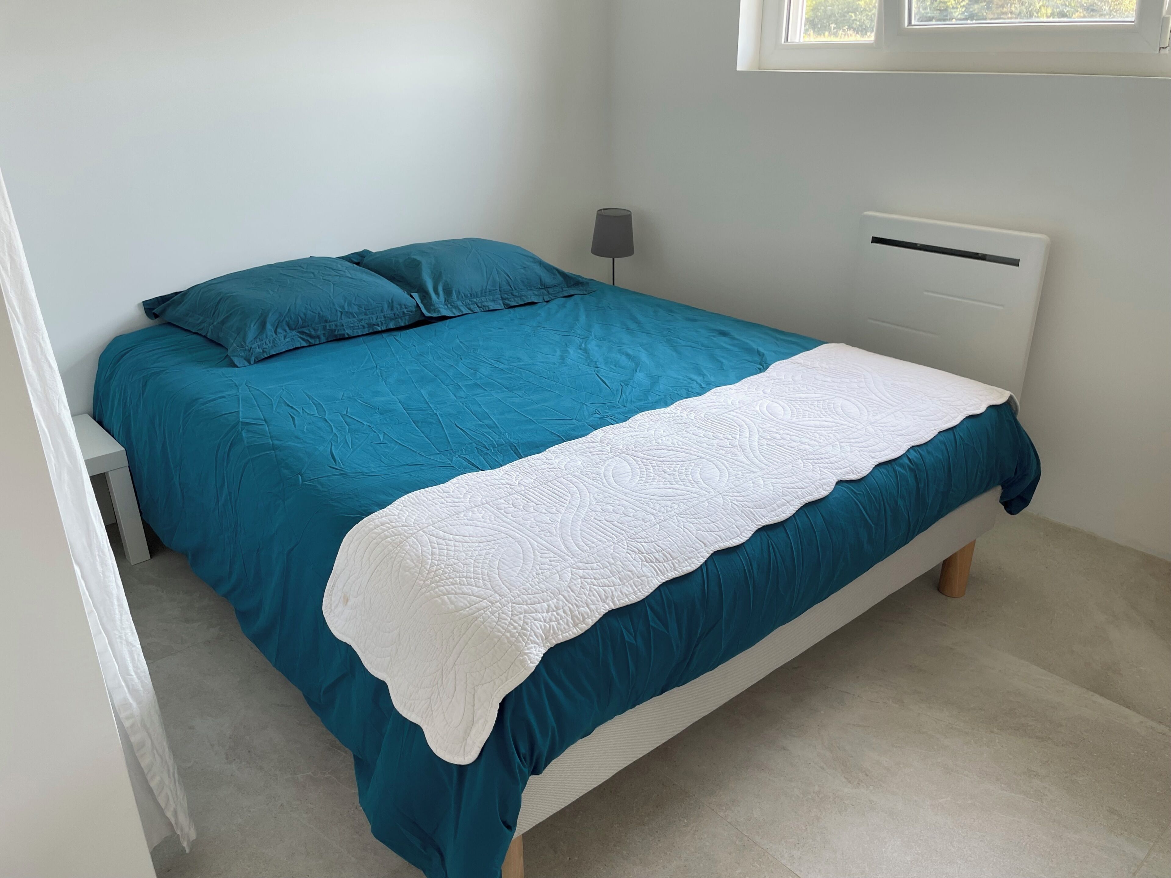 Un lit avec une couvre-lit turquoise et une couette blanche, une lampe de chevet et un radiateur.