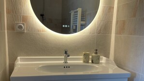 Een badkamer met een witte wastafel, een ronde spiegel en een handdouche.