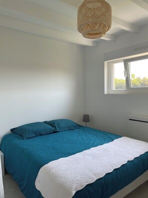 A bedroom with a bed, a window, and a hanging light fixture.