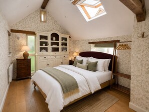 Een slaapkamer met een schuine kap, dakraam, een bed met witte beddengoed, een houten dressoir en een kast met glazen deuren.