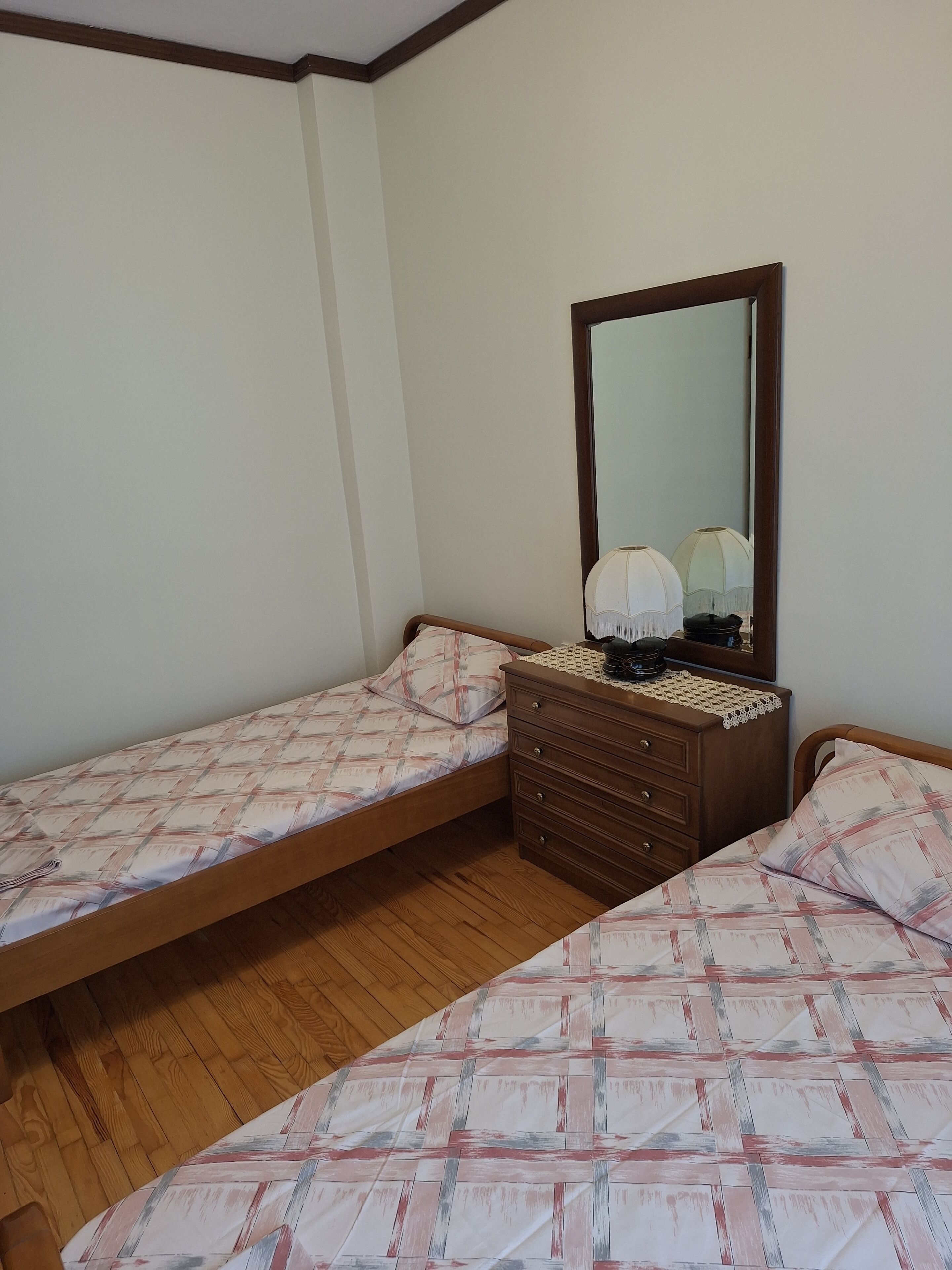 A bedroom with two single beds, a wooden dresser, a mirror, and a lamp.