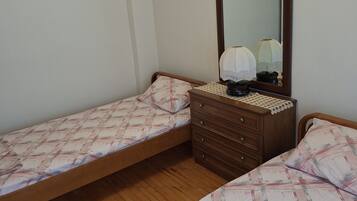 A bedroom with two single beds, a wooden dresser, a mirror, and a lamp.