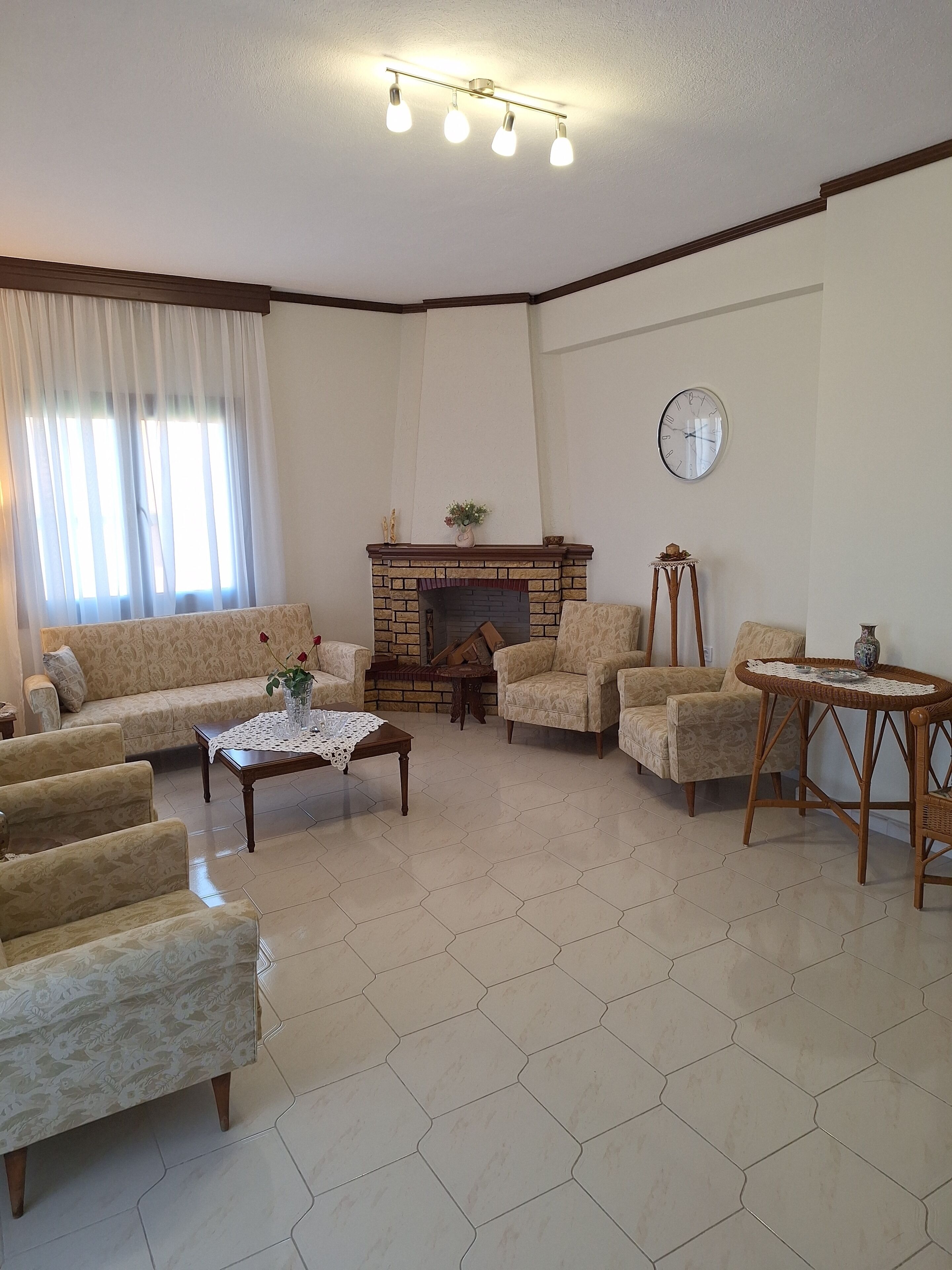 A living room with a fireplace, patterned sofas, a coffee table, and a clock on the wall.