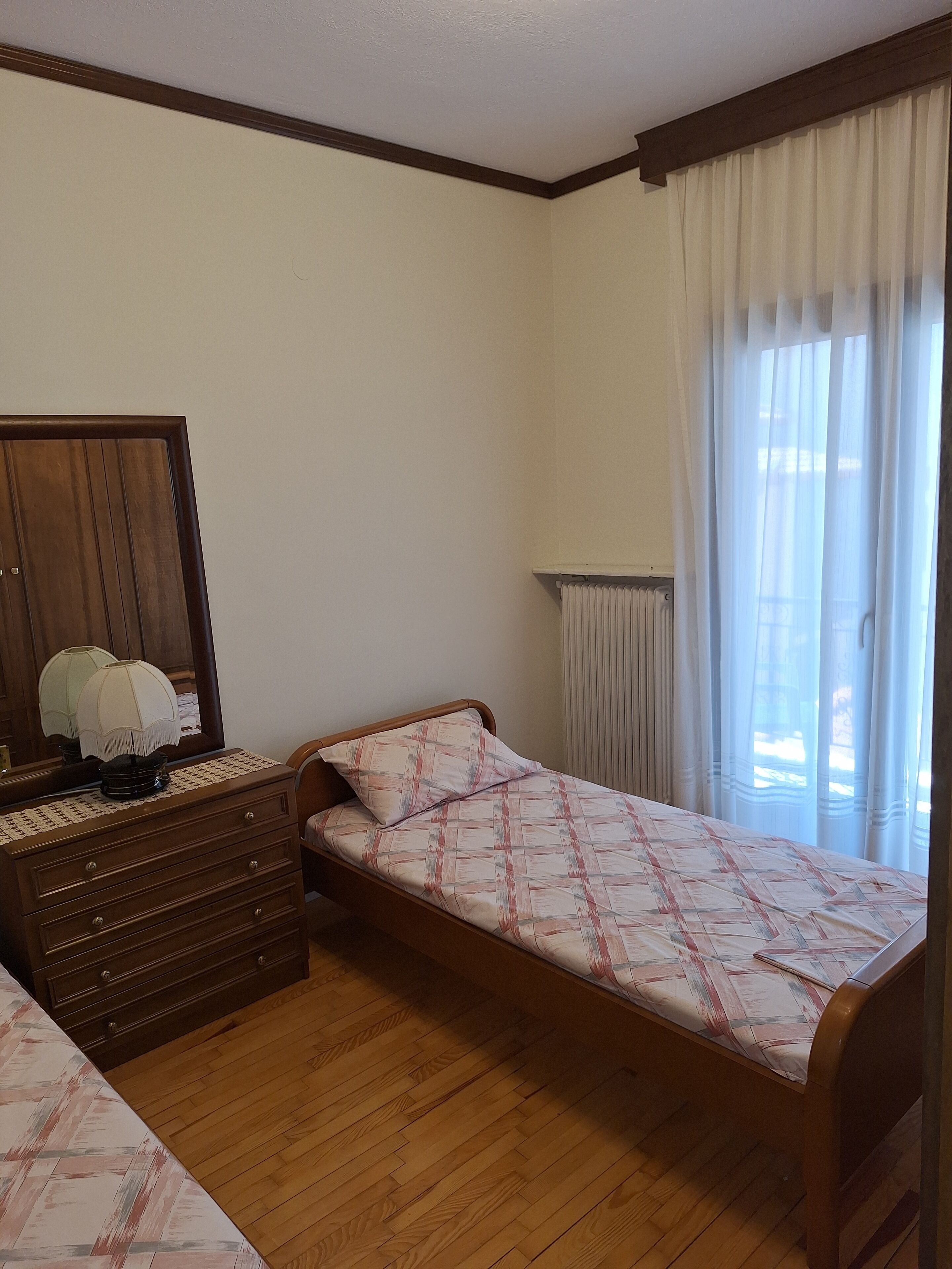 Quarto com cama de madeira, penteadeira com espelho e radiador.