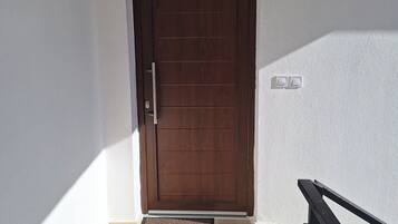 A closed wooden door with a metal handle, a small wall-mounted light fixture above it, and a doormat at the entrance.