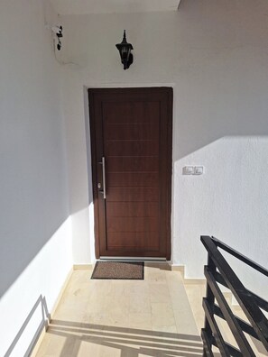 A closed wooden door with a metal handle, a small wall-mounted light fixture above it, and a doormat at the entrance. - Quiet apartement in Litochoro with panoramic view (Litochoro)