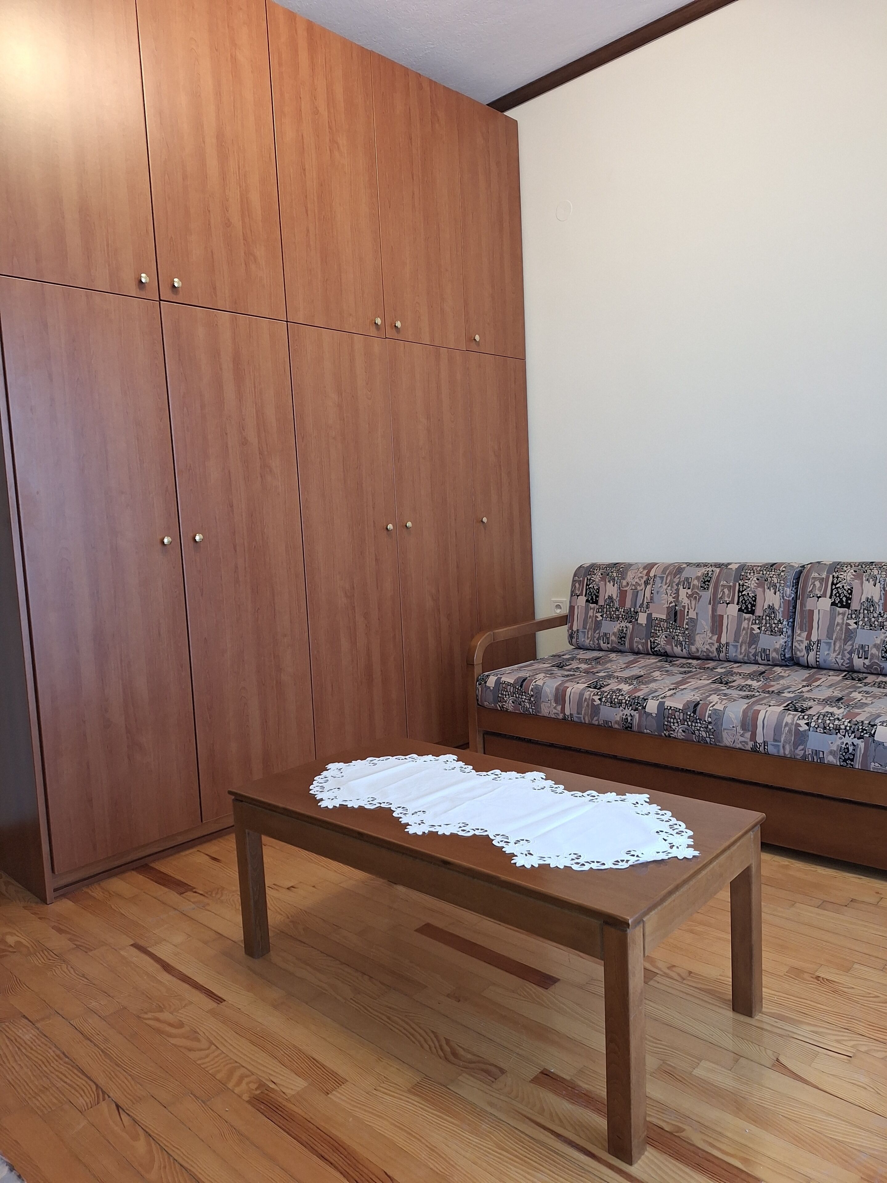 Una habitació amb un armari de fusta, un sofà estampat i una taula de centre de fusta amb un corredor de taula de renda.